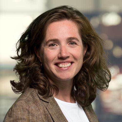 A picture of Anne Fleur van Veenstra. A smiling woman with dark hair standing in front of a blurred background