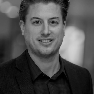 A black and white picture of Freek de Haan. He is standing in a hallway and smiling