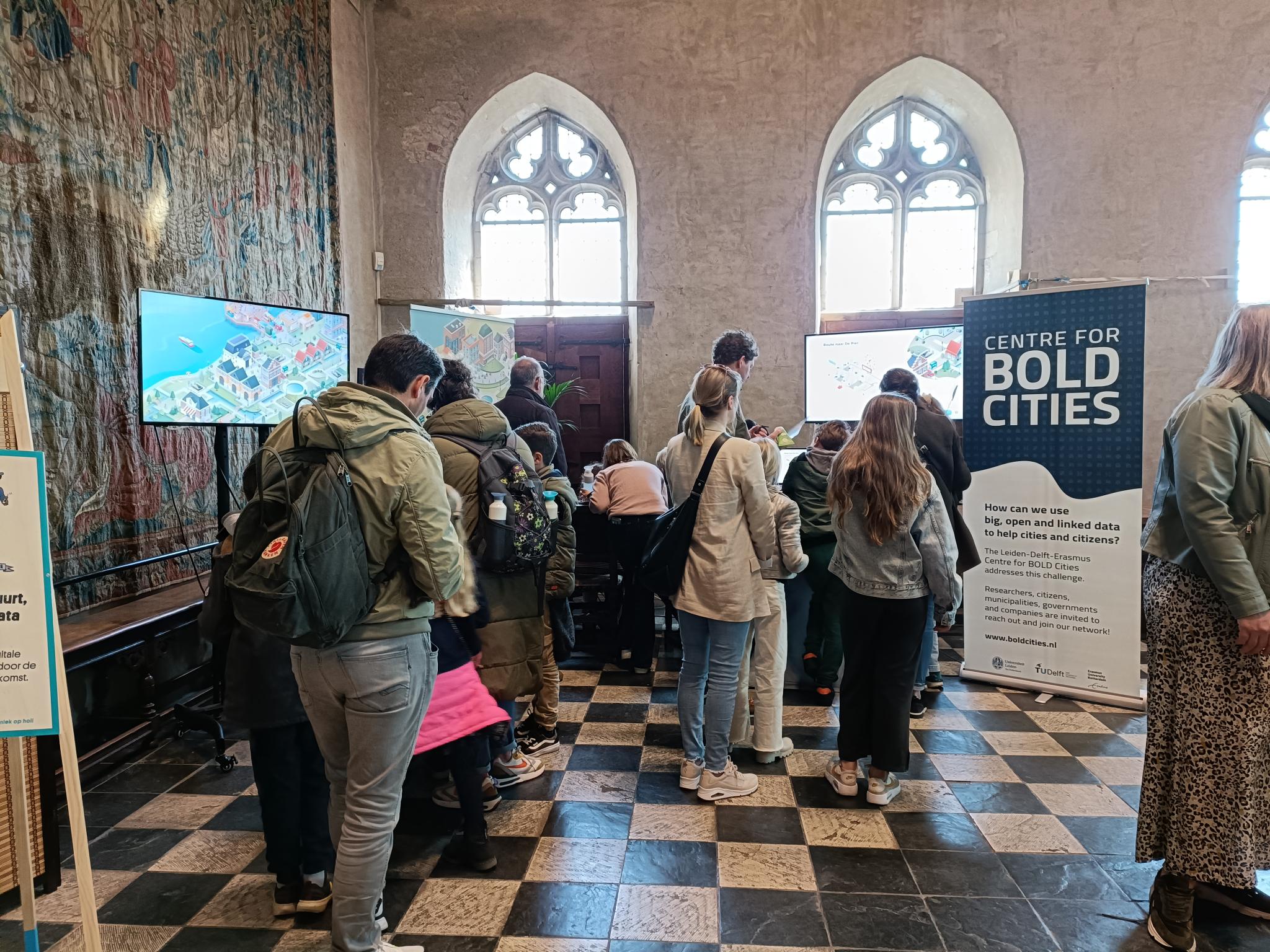 At Expeditie NEXT. Childrens and their parents in front of screens and banner with name: Centre for BOLD Cities