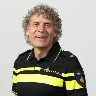 A picture of Wilco Berenschot, A man with grey hair standing in front of a light grey background wearing a Dutch police uniform