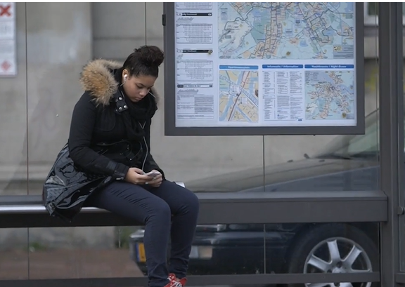 Meisje aan bushalte op haar mobiel