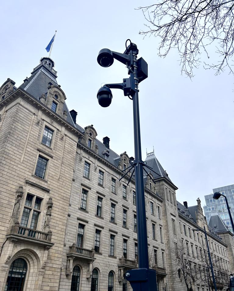 Een foto van een 'datapunt'. Een paal met meerdere veiligheidscamera er aan bevestigd. Op de achtergrond het Rotterdamse stadhuis.