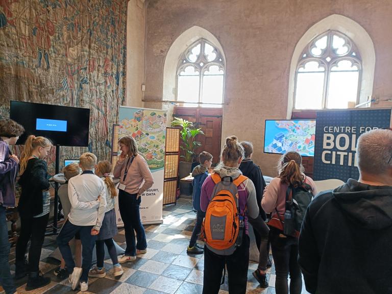 At Expeditie NEXT. Childrens and their parents in front of screens and banner with name: Centre for BOLD Cities