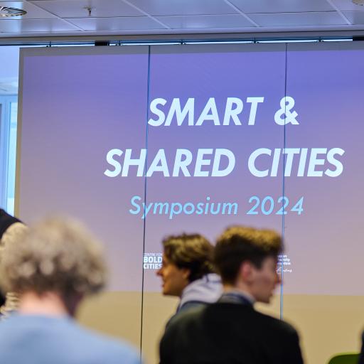 A picture of the event. A presentation is shown with the text "Smart and SHARED Cities". 