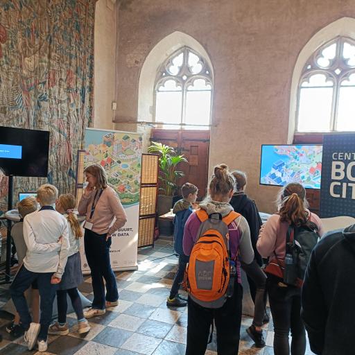 At Expeditie NEXT. Childrens and their parents in front of screens and banner with name: Centre for BOLD Cities