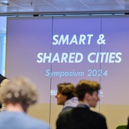 A picture of the event. A presentation is shown with the text "Smart and SHARED Cities". 